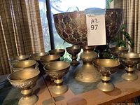 Wide view of metal punch bowl and ten matching goblets showing details of embossed floral patterns and bowl shape