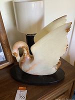 Full view of the swan sculpture lamp on black base with white lampshade