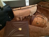 Five leather briefcases and bags displayed together showing variety of colors, styles and condition.