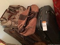 Stack of four luggage pieces: tan duffel, camel suede tote, brown soft rolling suitcase, black hard-shell rolling suitcase