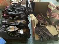 Photo of satin brown and black jacket with matching Kufi hat and folded textiles and blankets in a box.