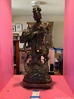 Front view of jade Quan Yin statue on wooden stand against pink background
