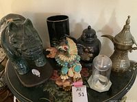 Overview of all items: green ceramic rhino, small glass rhino figurine, Kachina doll, black cylindrical vase, peacock ginger jar, brass oil lamp, glass dome cloche on hexagonal base