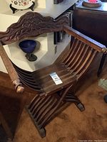Full view of the dark wooden Savonarola style armchair showing ornate backrest carving, curved slatted seat, and X-frame base.