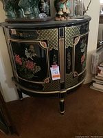 Front and angled views showing floral and bird hand-painted motifs on black enameled wood side table/cabinet with two doors and gold accents.
