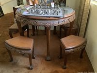 Distant view of round carved wood table with glass top and four matching benches nested beneath