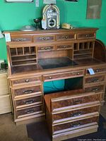 Front view of roll-top desk open to show desktop surface, drawers, chair partially visible