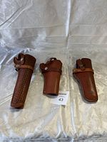 Three brown leather holsters arranged side by side on a white cloth background.