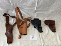 Four holsters on a cloth surface showing two larger shoulder holsters and two smaller holsters.