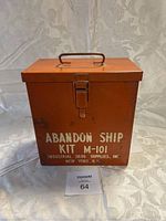Front view of the orange metal abandon ship kit box with handle and printed markings.