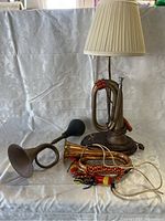 Display of the bugle lamp with beige lampshade and two vintage bugles, one with black bulb horn and one brass with cords