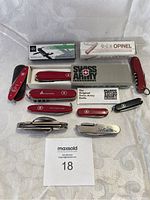 Lot of 11 Swiss Army knives and other multi-tools, some in original packaging, displayed on table.