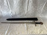 Full view of the sword and its sheath laid on a patterned white fabric showing the black wrapped handle and rounded pommel.