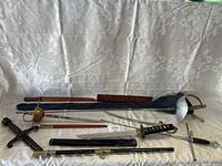All 5 swords displayed on white fabric, some with sheaths and cases in background