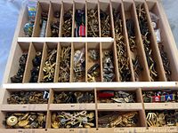 Wooden drawer organizer with multiple compartments filled with various military pins, medals, ribbon bars, and buttons mainly in gold and silver tones.