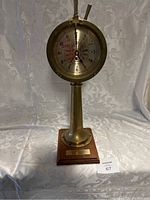 Full view of brass engine order telegraph clock standing on wooden base with a hanging white tag numbered 67.