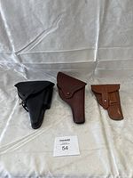 Three leather gun holsters side by side on a white fabric background: black, dark brown, and light brown.