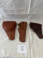 Three leather gun holsters side by side on a white cloth background.