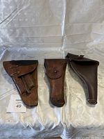 Three worn vintage military leather holsters laid out flat on fabric background.