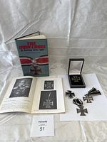 Overview: one hardcover history book, open reference book pages, four Iron Cross medals laid out on white background with lot tag