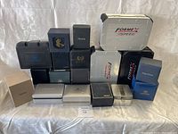 Wide shot of 18 various branded watch boxes arranged in 3 rows on fabric background.