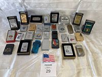Wide view of 32 assorted lighters laid out on cloth with belt buckle and lapel pin visible