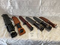 Wide view of six sheathed fixed blade knives on fabric background