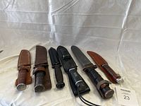 Six knives lined up with sheaths on white background