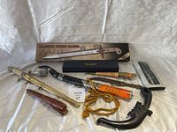 Photo showing all nine items including Marine dress saber in box, several daggers and knives with sheaths, some in boxes or protective cases, arranged on a fabric backdrop.