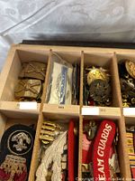 Wooden compartment tray filled with multiple slots of brass buttons, pins, stripes and more.