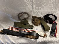 Photo showing five belts and straps laid out on a white textured fabric background, highlighting the different belt types and materials.