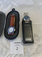 Front view showing Nautica watch with brown leather strap and blue bezel alongside Swatch Irony Chrono watch in leather holder case