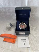 Nautica men's chronograph watch with orange subdials in the original blue Nautica box, additional orange rubber strap and stainless steel bracelet links in plastic bags placed next to the box.