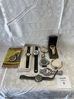 Overview of the random watch bundle displayed on a white cloth background showing all watches and wristwatches including boxed Medana watch, The Precise Jogger, and two gold-tone bangle watches.