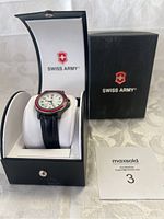 Swiss Army wristwatch displayed on white cushion inside black presentation box, with black outer box and maxsold lot tag visible.