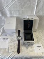Full lot overview including watch, metal case, white outer box, papers and receipt on a white patterned cloth background.