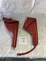 Two US military leather holsters placed on white fabric with MaxSold lot number card