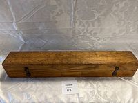 Closed wooden storage case made of medium-toned wood with metal latch clips on the front and an indented label plate area.