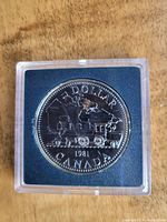 Front side of the 1981 Canadian silver dollar coin showing a steam locomotive train design with text indicating its face value, year, and country.