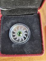 Front view of 2011 $3 Canadian silver coin featuring a green August birthstone set in a swirl design inside a red velvet box with black interior.