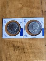 Obverse side of two 1971 US Kennedy half dollar coins showing President Kennedy's profile, both in protective holders with markings.