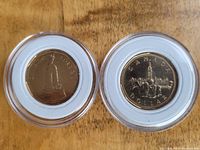 Both Canadian one dollar coins displayed obverse and reverse in clear plastic holders on wooden surface.
