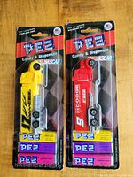 Photo of two NASCAR-themed PEZ candy dispensers in original blister packaging showing yellow Team Z and red Dodge #9 truck designs.