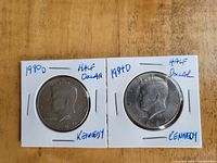 Front sides of 1980D and 1984D Kennedy half dollar coins in holders, showing Kennedy portrait and handwritten labeling.
