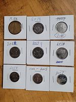 Nine Canadian coins in cardboard holders labeled with years, arranged in a 3 by 3 grid, coins vary in size and design, showing wear consistent with circulated condition.