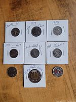 Photo showing nine Canadian coins labeled with years and some marked with specific annotations such as 'airplane' and 'V'. Coins are in circulated condition and mounted in individual cardboard holders.