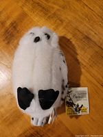 Plush white and black spotted snowy owl with tag attached.