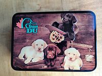 Decorative metal storage tin with a picture of four puppies and Team Ducks Unlimited logo on the lid.