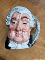 Close-up of the front of the Toby jug showing the character face with powdered wig, smirking expression, and quill pen detail.