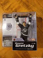 Front view of Wayne Gretzky McFarlane Legends figure sealed in box with arms raised, wearing black LA Kings jersey with number 99 and captain 'C'. Box includes NHL and Legends branding.